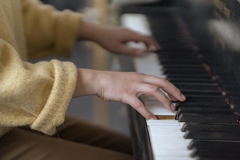 Side view of crop anonymous lady in casual outfit sitting in light room while playing piano